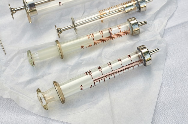 Photo vintage old medical glass syringes and needles on white linen fabric