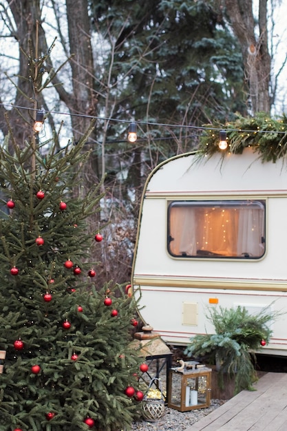 Vintage old travel trailer with Christmas decorations Christmas tree chair and Christmas lights Cozy home camping before Christmas holidays