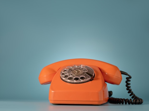 Vintage orange telephone on blue wall