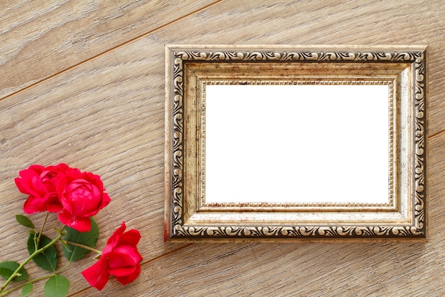 Vintage photo frame with copy space and red roses on wooden boards. Top view.