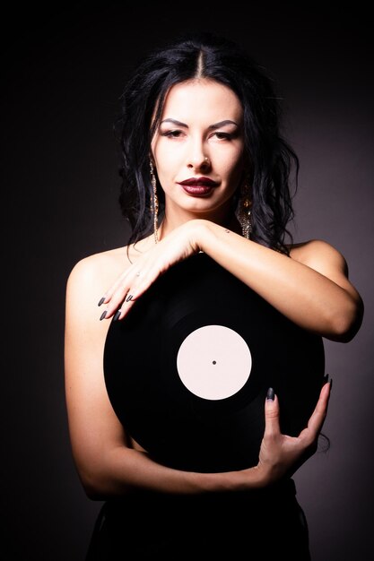 Vintage photo of a glamorous pinup girl holding a vinyl record and looking up on a pink background