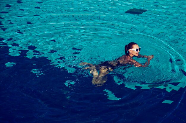 수영장에서 수영하는 검은색 수영복과 흰색 선글라스를 쓴 여성의 빈티지 사진