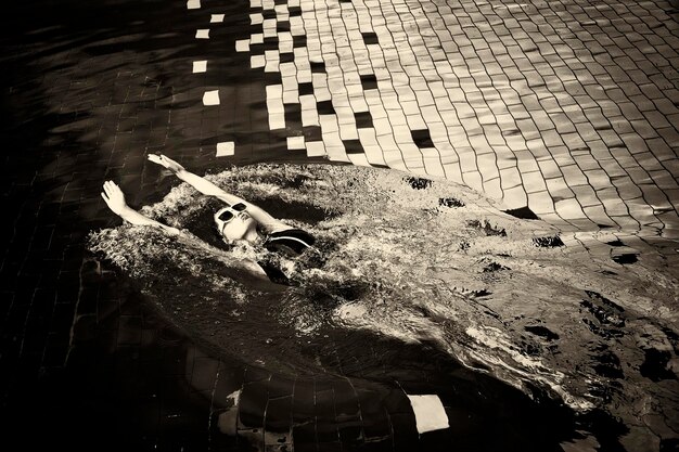 Винтажное фото женщины в черном купальнике и белых солнцезащитных очках, плавающей в бассейне