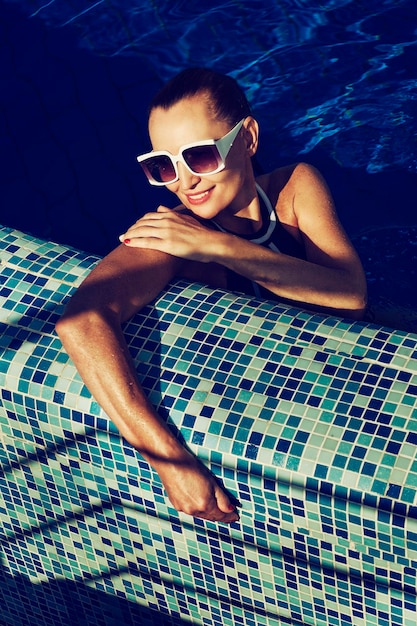 Винтажное фото женщины в черном купальнике и белых солнцезащитных очках, плавающей в бассейне
