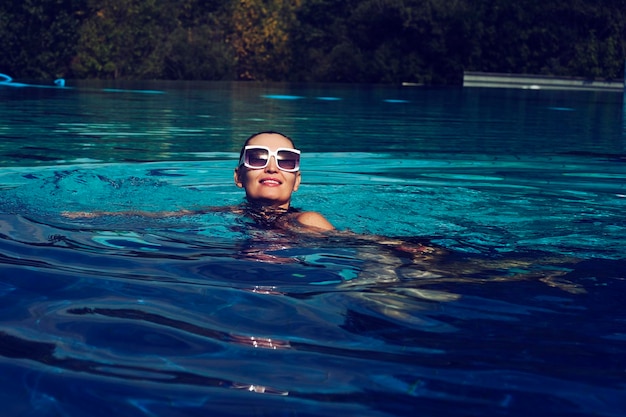 Vintage photo of a woman in a black swimsuit and white sunglasses swimming in the pool