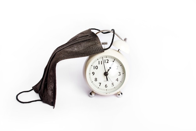 Vintage pink alarm clock with a face mask. Time until the end of quarantine, find a vaccine or new normal global concept. High quality photo