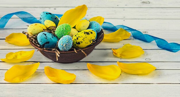 Vintage plate with blue and yellow easter eggs and tulip petals on a light wooden background