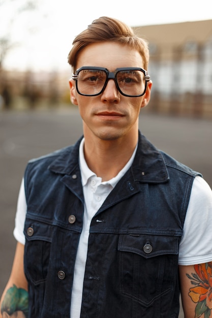 Старинный портрет красивого молодого человека в очках и джинсовой одежде на улице