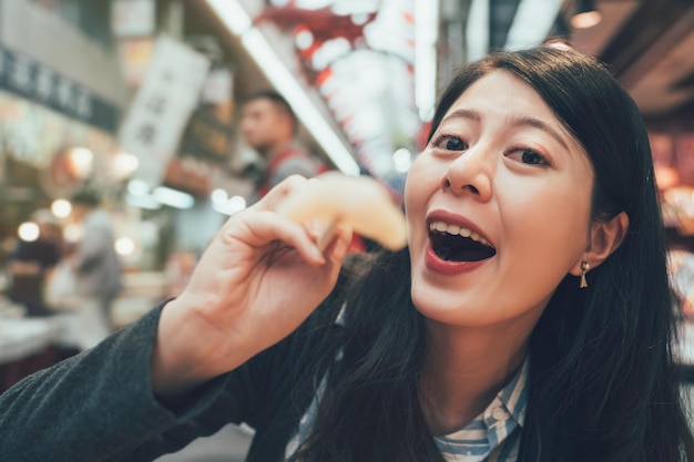 vintage portrait of happy local woman showing camera using chopstick eat japanese local fresh sea food fish sashimi sitting at vendor restaurant indoor kuromon ichiba traditional market osaka japan.