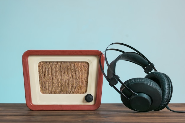 Vintage radio and headphones on a wooden table on a blue background. Technique for sound and video reproduction.