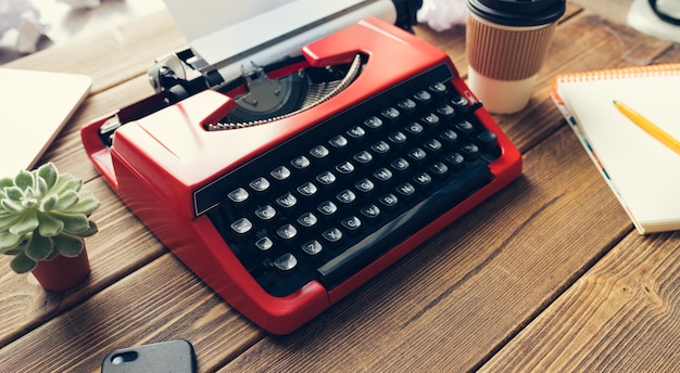 Vintage red typewriter machine on the old wooden working desk