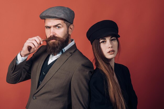 Photo vintage retro couple on red wall old style hat on bearded man and black fashion cap on beauty woman