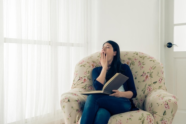 Pellicola vintage retrò foto a colori di bella bellezza modello femminile seduto su un comodo divano leggendo il libro del diario sentirsi stanco sbadigliando nel soggiorno di casa.