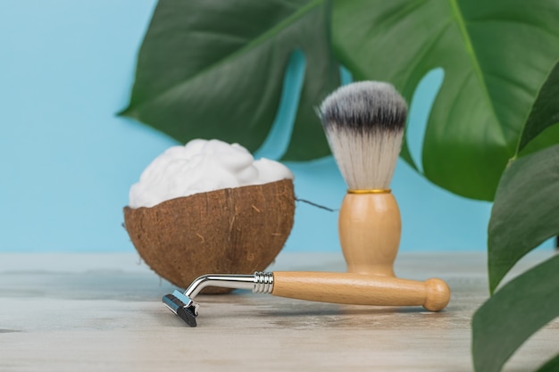 Vintage shaving accessories on a blue background with a large sheet of monstera.