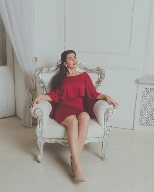 Vintage sitting chair posing attractive girl in a red dress.