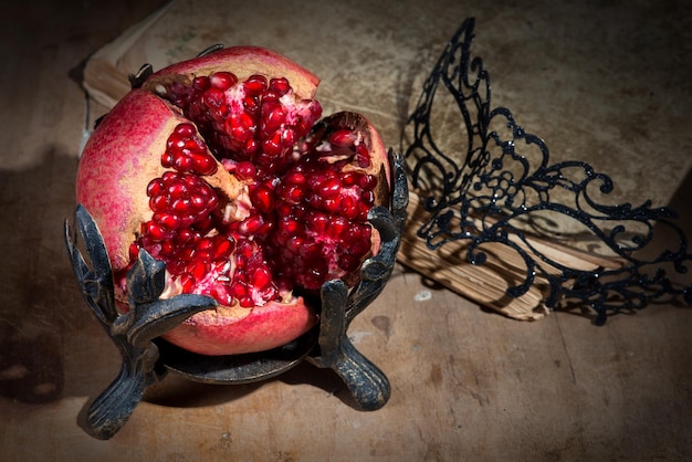 Vintage still life with pomegranate lacy mask and ancient book on wooden table