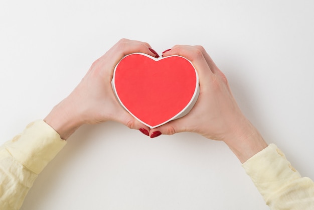 Vintage style red heart shaped box in female hand on white background.