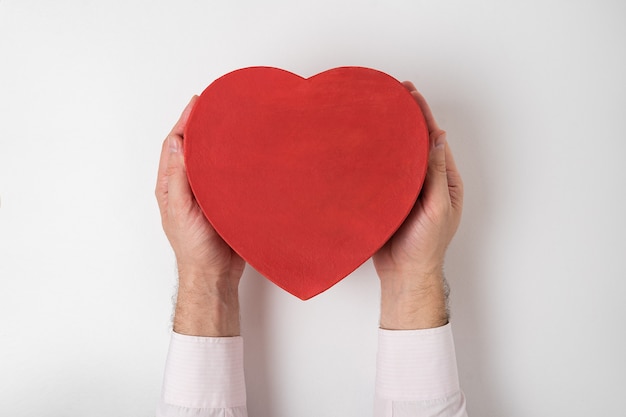 Vintage style red heart shaped box in male hands isolated on white background