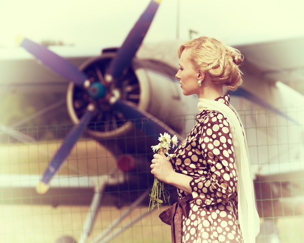 Vintage stylized photo of beautiful girl with a bouquet of daisies and plane on background