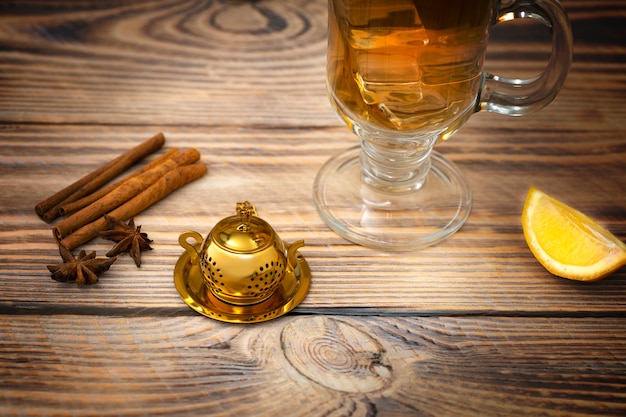 Vintage tea strainer and glass of tea on a wooden table with lemon and cinnamon