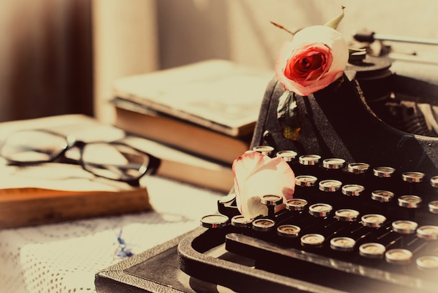 Vintage typemachine met roze roos, oude boeken op tafel.