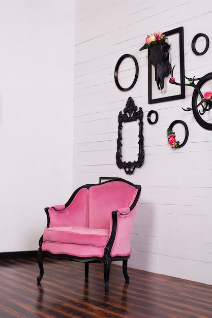 Vintage velours fauteuil, in een lichte kamer. Diverse lege fotolijsten met een schedel en geweien opknoping op een houten muur. Het concept van wanddecoratie. Decor, vintage, modern, loft. gotische stijl
