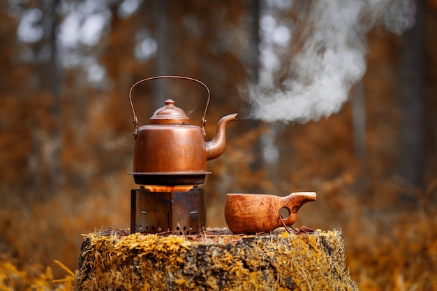 Vintage waterkoker met koffie op het fornuis en een houten kopje op een oude boomstronk in bos