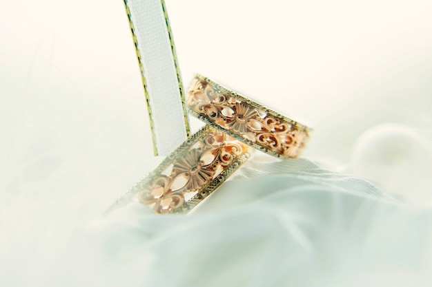 Винтажные обручальные кольца среди белых лент, конец-вверх. Золотые кольца с узорами на размытом белом фоне. Свадебные и семейные традиции.