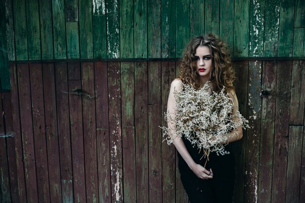 Vintage woman as witch, posing against abandoned place on the eve of Halloween