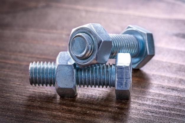 Vintage wooden board with pair of metal threaded bolts and nuts construction concept