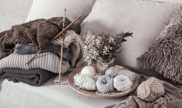 Старинные деревянные вязальные спицы и нитки на уютном диване с подушками и вазой с цветами