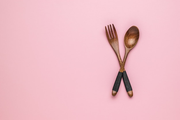 Vintage wooden spoon and fork on pink background. Space for text.