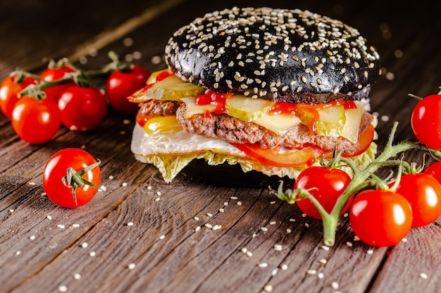 Foto tavolo in legno vintage, su un tagliere, hamburger succoso pane nero scuro, formaggio, fette di carne di maiale