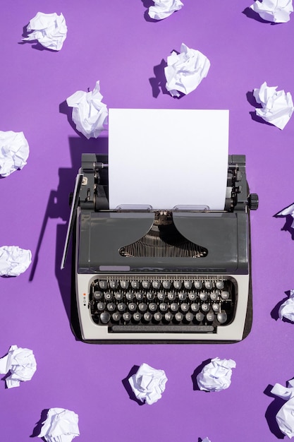 Vintage writing machine with a blank sheet of paper and multiple creased pages on violet background