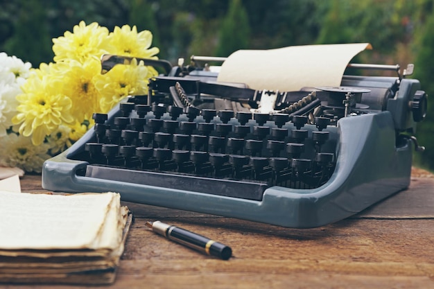 Vintage zwarte typemachine met oude boeken en bloemen op houten tafel buitenshuis