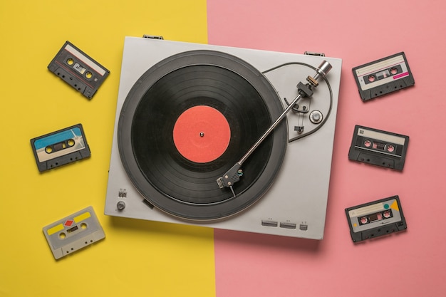 Vinyl record player and tape recorders on a yellow and pink background.