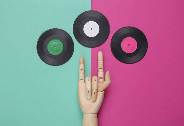 Vinyl records and wooden hand showing Rock gesture on pink blue background Top view Minimalistic music concept Rock'n'roll