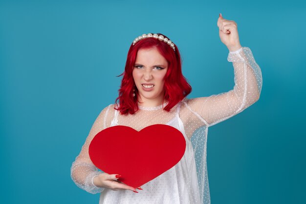 Violent woman holding a big red paper heart and waving, shaking her fist that will hit