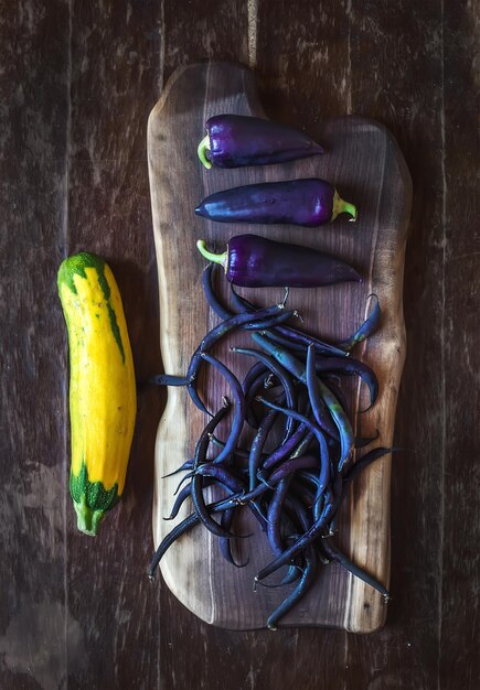 Violet chili pepers bonen en gele courgette op rustieke houten snijplank over donkere houten achtergrond