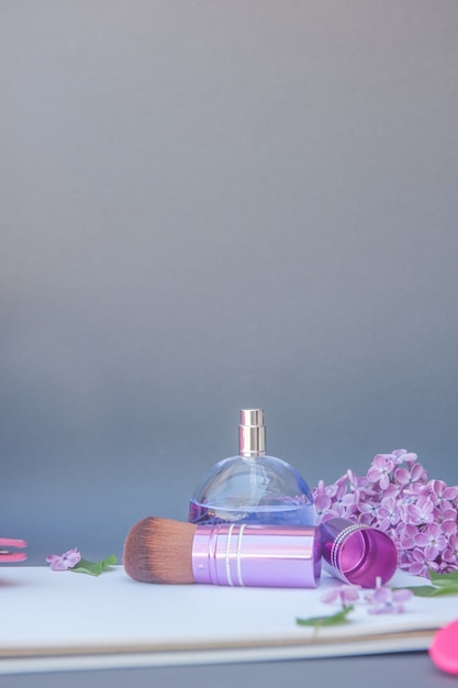 Violet cirkel parfumflesje en make-up borstel met verschillende bloemen, verticale plaats voor tekst