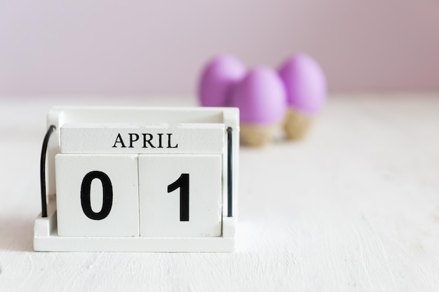 Photo violet eggs on a white vintage background next to it a wooden calendar with the date of april 1