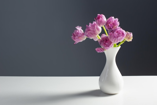 Violet tulips in white vase on background gray wall