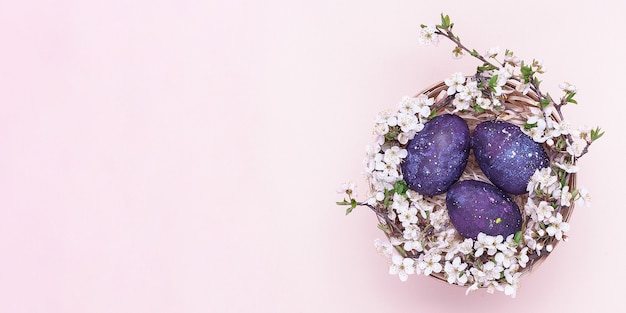 Violette paaseieren in een mand met bloemen op een roze achtergrond.