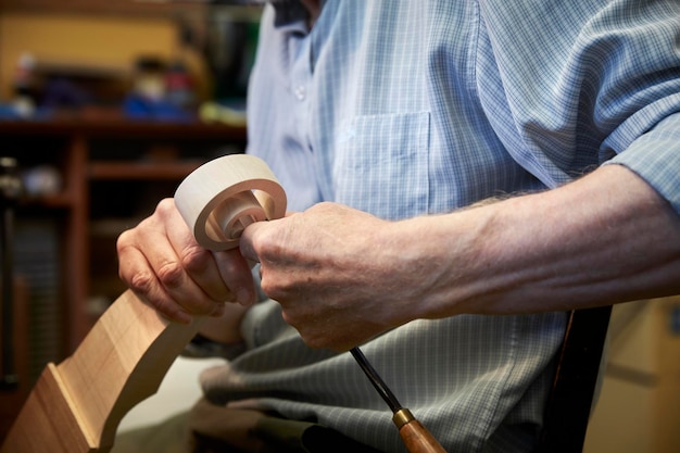 A violin maker using hand tools to smooth and finish a new wooden vioin headstock, curled scroll of