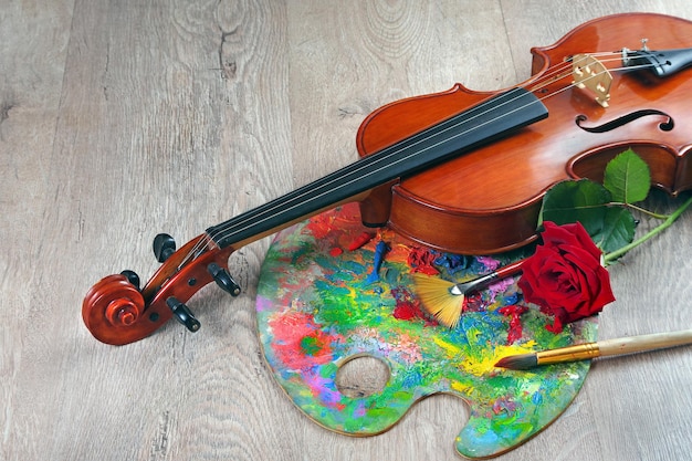 A violin sits on a wooden floor with a red flower on the top.