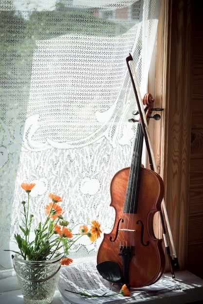 Violin with sheet music and flowers on windows.