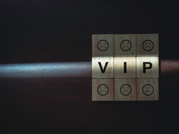 Vip words and boring faces emoticon on wooden blocks with the\
light on dark wood background with copy space. privileges\
infringing on other people freedoms and civil liberties\
concept.