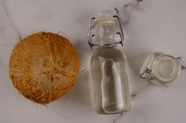흰색 대리석 테이블에 있는 병에 담긴 버진 코코넛 오일 또는 VCO. 코코넛 껍질. 코코넛. 콜드 프레스.