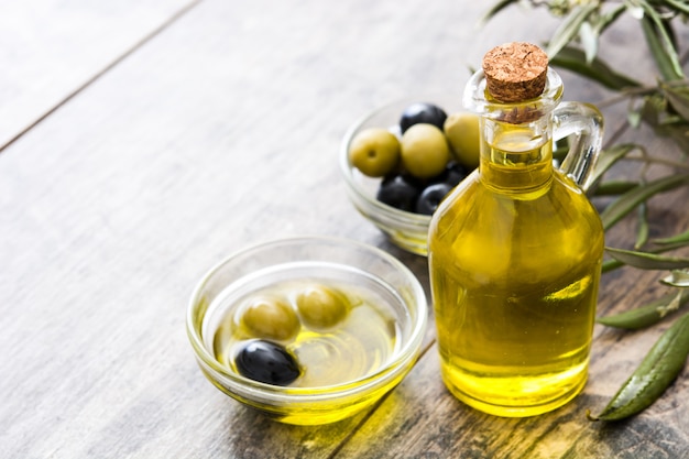 Olio d'oliva vergine in una bottiglia a cristallo sulla tavola di legno