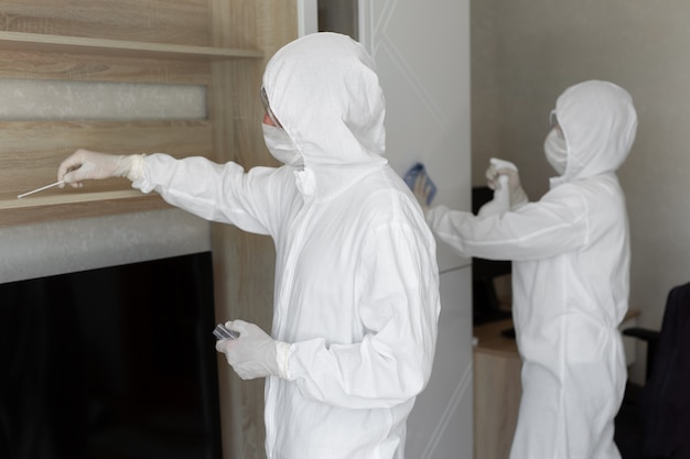 I virologi, le persone in tuta protettiva eseguono la disinfezione nell'appartamento. pulire i mobili e prelevare campioni per la contaminazione dalla superficie durante un'epidemia di coronavirus. covid-19
